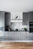 Offene Küche mit grauen Schrankfronten und weißen Spritzschutzfliesen