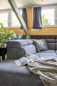 Grey upholstered sofa over with plaid pattern, magazine, and throw pillows