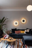 Wall lamp above sofa with velvet upholstery, side tables and indoor plant