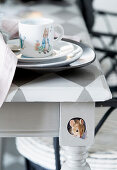 Place setting on table with chequered top and little trompe l'oeil mouse painting on one leg