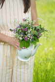 Woman holding porcelain pot with bouquet of meadow flowers