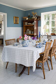 Gedeckter Tisch mit Rattanstühlen und Geschirrregal im Esszimmer mit blauen Wänden und weißen Fliesen
