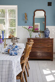 Gedeckter Tisch mit Rattanstühlen und Kommode im Esszimmer mit blauen Wänden und weißen Fliesen