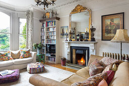 Spiegel mit vergoldetem Rahmen auf Kaminsims, Bücherregal und Sofas im Wohnzimmer mit Stuckdecke