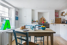 Weiß gestrichene Küche mit bunten Accessoires, Tisch mit Stühlen in der Mitte