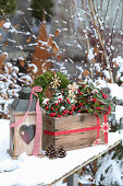 Winterliche Dekoration mit Holzkiste, Ilex, Strohsternen und Laterne im Schnee