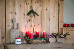 Advent wreath made from fir branches with red candles in front of a wooden wall