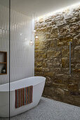 A free-standing bathtub in a bathroom with a sandstone wall