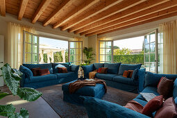 Blaue Polstergarnitur vor geöffneten Terrassentüren im Zimmer mit Holzbalkendecke