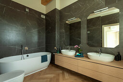 A washstand with two countertop sinks and mirrors, and a freestanding bathtub in a bathroom with marble tiles
