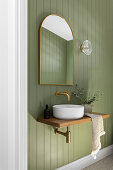 Small vessel sink, above it a arched mirror on a green painted wood paneled wall