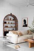 Travel souvenirs in an arched wall niche, in front bright, comfortable upholstered sofa in the living room