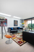 Schwarze Ledercouch, Stativlampe und Vintage Stuhl in hellem Wohnzimmer mit Terrassenzugagn