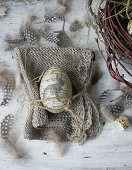 Deco egg on knitted napkin surrounded by quail feathers