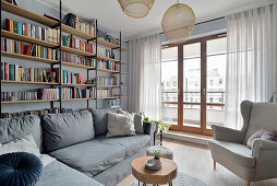 Sitting area with grey sofa and armchair in front of floor-to-ceiling shelf and balcony door