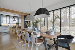 Long dining table with various chairs, above hanging lamps in front of glazing in open living area