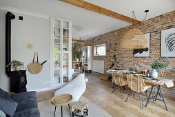 Open living room with dining table in front of brick wall, woven pendant light above it