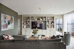 Graue Sofagarnitur, großformatiges Gemälde an der Wand und Regalschrank im Wohnzimmer mit raumhoher Verglasung