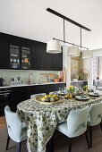 Long, oval dining table and upholstered chairs in kitchen with dark cupboards