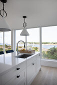 White kitchen island in front of wall of windows, view of coastal landscape