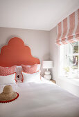 Double bed with generous, coral-colored headboard, flanked by bedside tables with white lamps