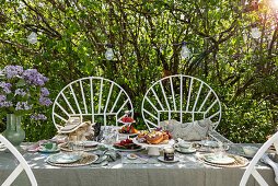 Gedeckter Tisch zu Tea Time unter Fliederstrauch im Garten