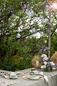 Gedeckter Tisch unter Fliederstrauch im Garten