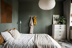 Double bed and white bureau in bedroom with green walls
