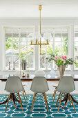 Verglaste Veranda mit Esstisch und weißen Klassikerstühlen auf türkisblauem Teppich