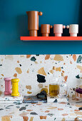 Küchenarbeitsplatte und Spritzschutz aus Marmorterrazzo, darüber Regal an blauer Wand