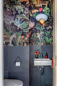Gäste-Toilette mit grauen Wandfliesen, darüber Tapete mit Dschungelmotiv