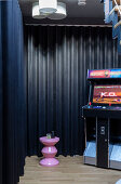 Arcade game machine and pink stool in front of black wall