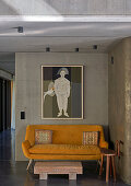 Yellow sofa and wooden stool in front of concrete wall with artwork