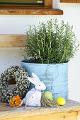 Rosemary pot surrounded by Easter decorations and wreath of pussy willows on wooden bench