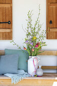 Spring bouquet of freesias and tulips (Tulipa) next to cushion on wooden bench