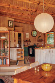 Dining area and kitchen with wood-paneled walls and rustic furnishings and paper lamp