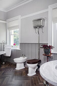 Toilette, Spülkasten mit Nickel-Finish und Bidet im Badezimmer mit Bodenfliesen in Holzoptik