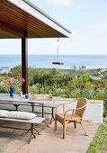 Überdachte Terrasse mit Tisch, Sitzbänken und Rattanstuhl, Blick auf das Meer