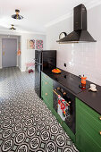 Dunkelgrüne Unterschränke mit schwarzer Konglomerat-Arbeitsplatte und geometrische Bodenfliesen in offener Küche