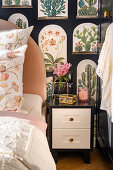 Bedroom with pink double bed, bedside table, and wallpaper with terrarium motif