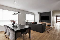 Open plan living room with black sofas, dining area with black wooden table and grey upholstered chairs