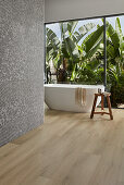 Modernes Badezimmer mit weißer, freistehender Badewanne und Blick auf tropischen Garten