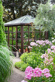 Glass house surrounded by flowering perennials and gravel path in the garden