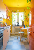 Orangefarbener Kühlschrank und rosa Schränke in Küche mit gelben Wänden