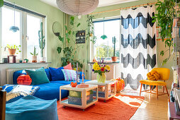 Eklektisches Wohnzimmer mit blauem Sofa, Couchtischen aus weißem Kunststoff und gemustertem Vorhang