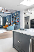 View over kitchen island to fridge and built-in appliances, living room with blue shelving wall in the background