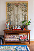Regal mit Decken, Kissen, Porzellan, Buch und Zimmerpflanze, darüber Wandbehang
