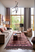 Upholstered sofa, colorful carpet and designer lamp in living room with floor-to-ceiling windows