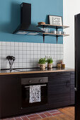 Küchenzeile mit dunklen Schrankfronten, darüber weiße Wandfliesen und blaue Wand