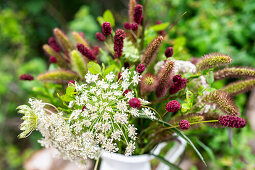 Sommergräser in Weiss und Rot in einer Vase vor grünem Blattwerk